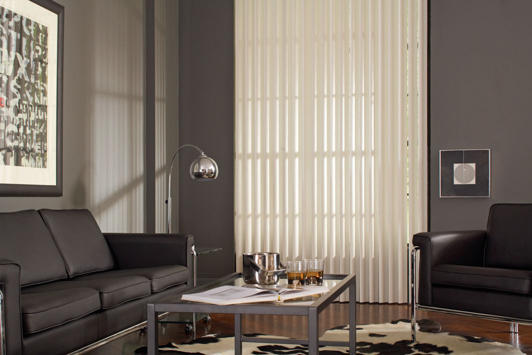 White Discoveries® Vertical Blinds in a room with gray walls and black furniture