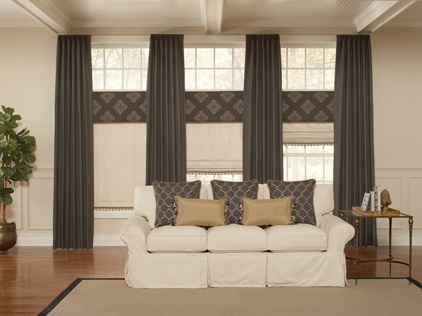 Dark brown Interior Masterpieces® Draperies with tan Fabric Shades, dark brown geometric patterned Fabric Wrapped Cornices, and matching Custom Pillows on a cream colored couch