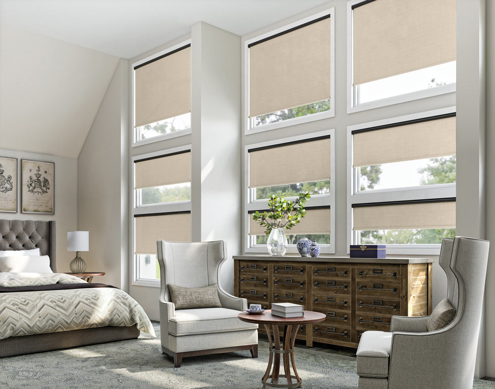 A grid of nine windows each with a tan Genesis® Motorized Roller Shade and a black headrail behind a large dresser and chairs