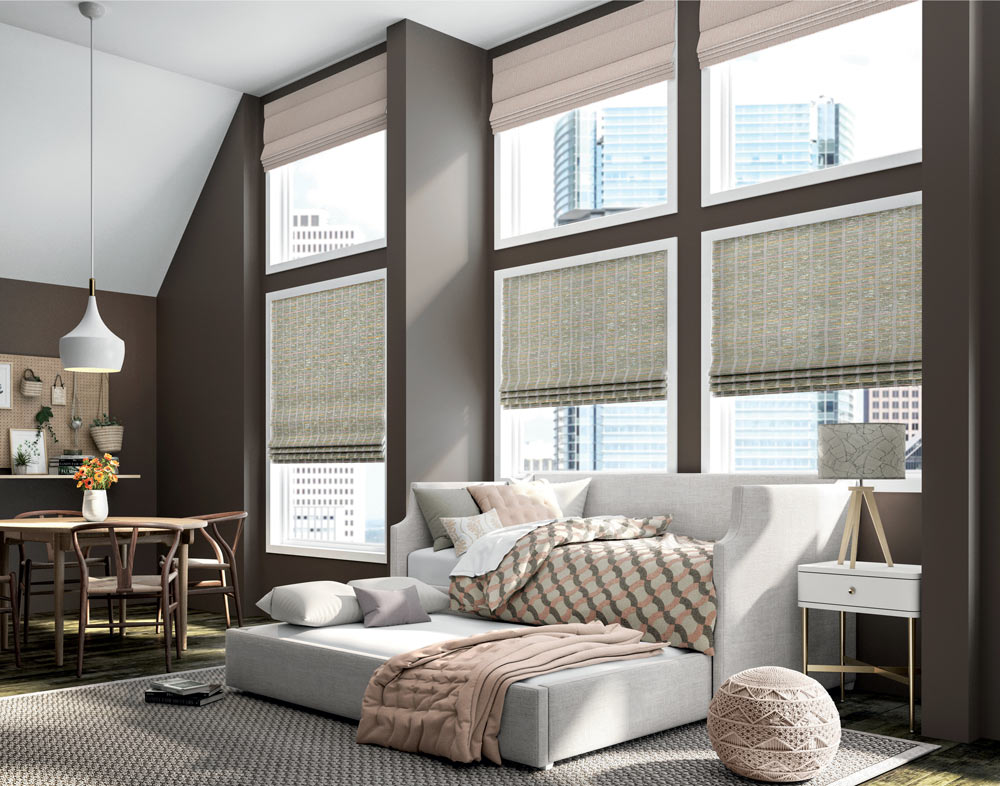 several large green Manh Truc® Hobbled Roman Shades underneath the same number of light pink Interior Masterpieces® Fabric Shades behind a couch and pull out sleeper that has custom bedding and pillows on it