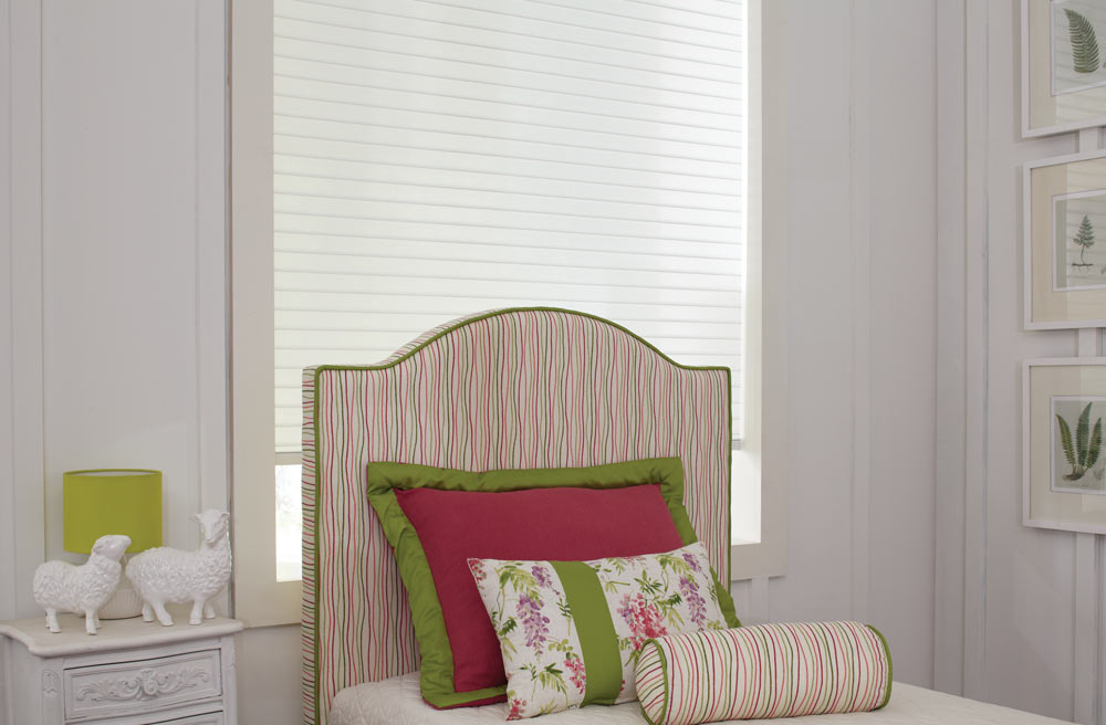 Large white Tenera® Sheer Shade behind a colorful pink, green, purple, and white Interior Masterpieces® headboard and matching pillows